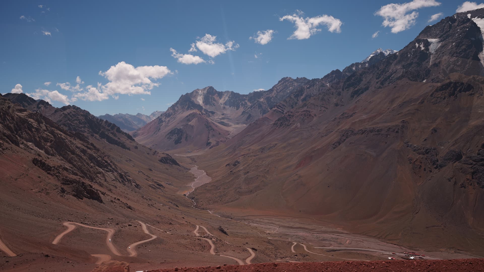 Winding roads through a wide red and brown Andes valley under blue sky