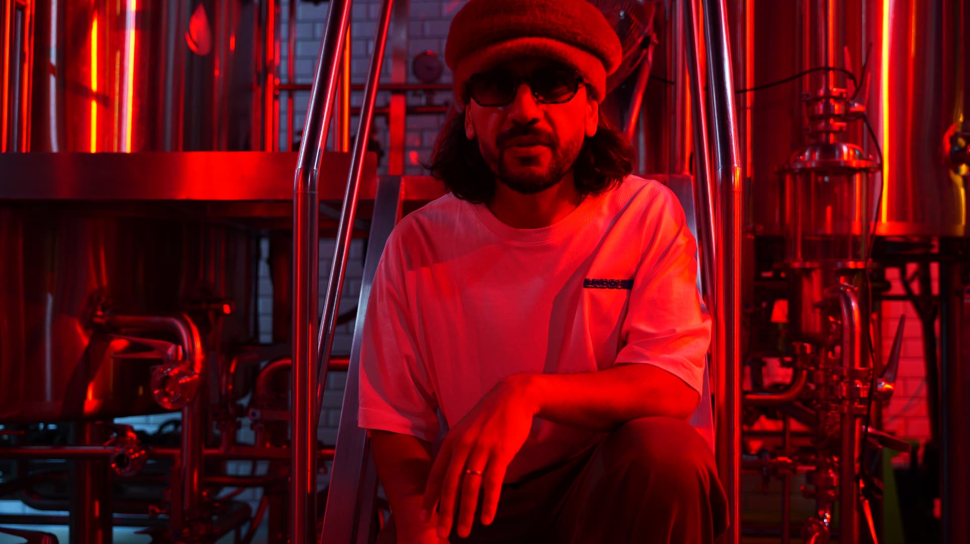 Close portrait of a man in a beret seated among brewery tanks in red light