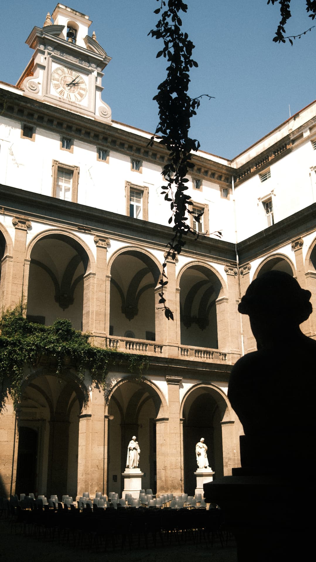Clock tower and arcaded courtyard of the University of Naples under a blue sky