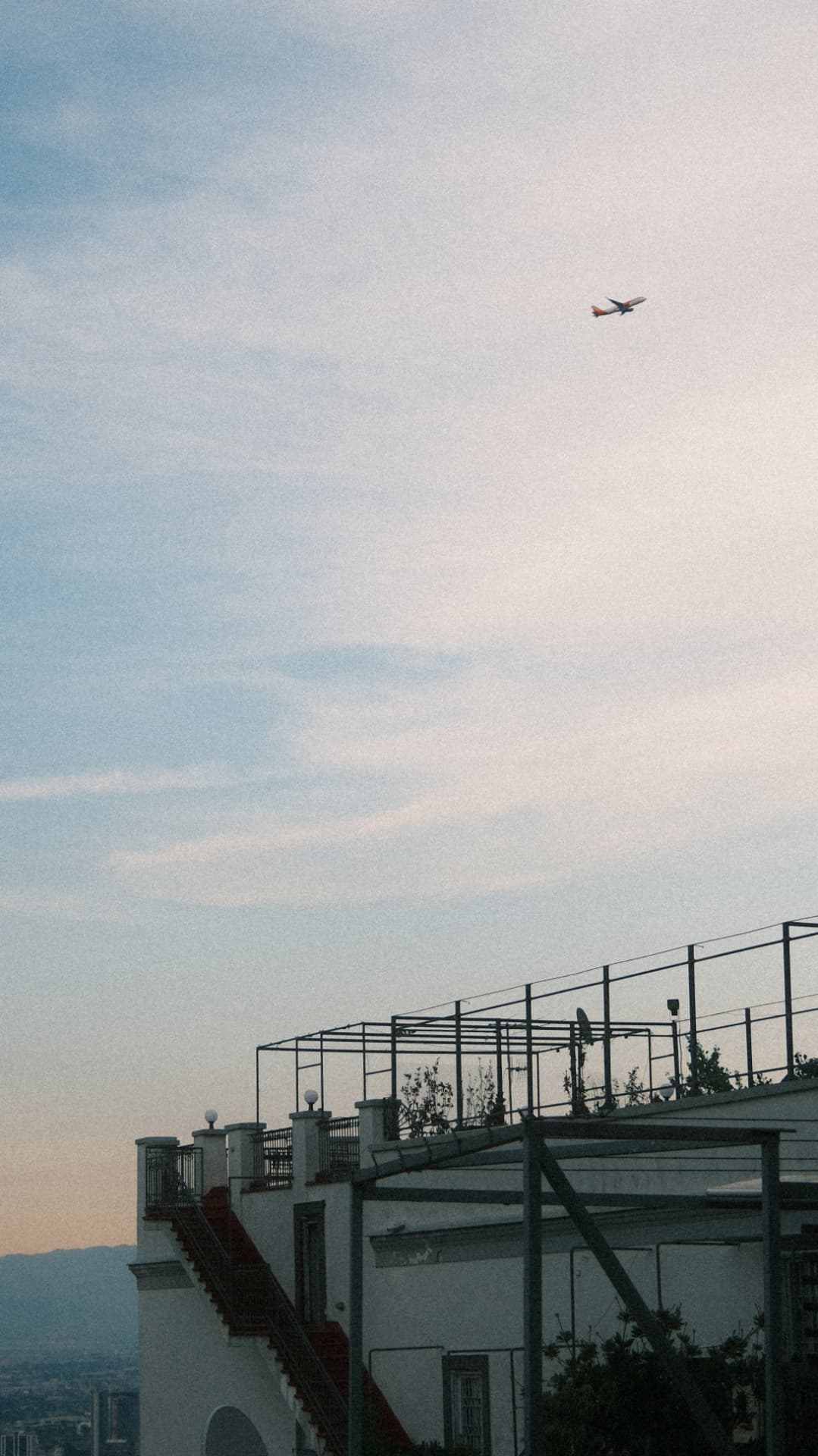 Plane crossing a pale dusk sky above a white rooftop terrace