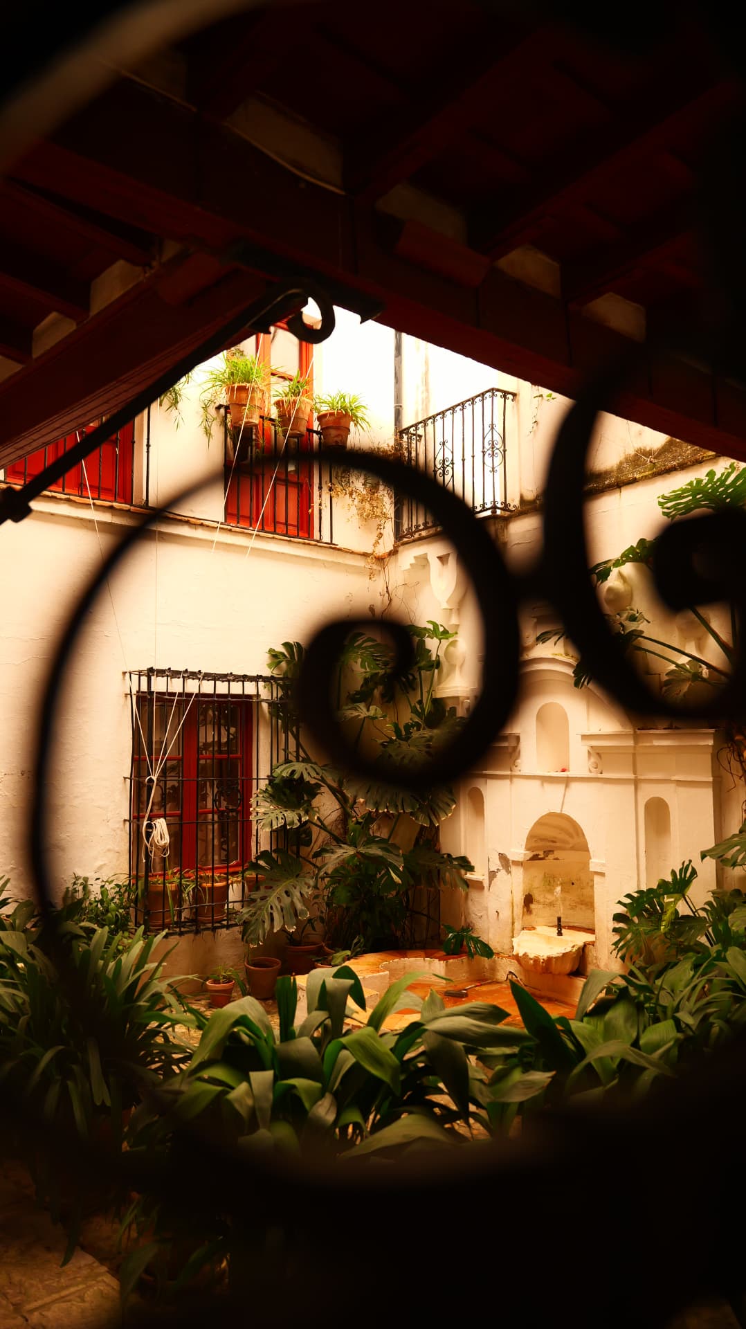 Andalusian courtyard with red doors, plants and a fountain seen through wrought-iron scrollwork