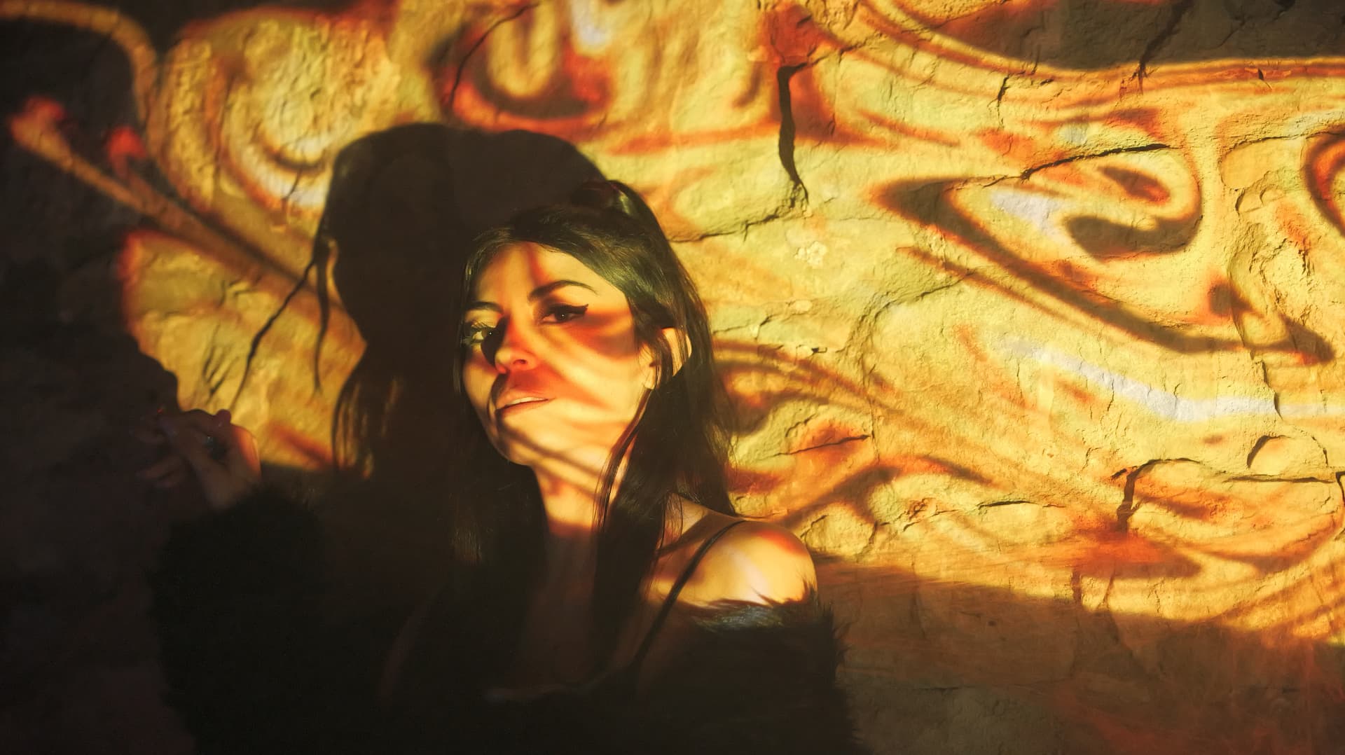 Woman lit by amber liquid-light projections on a cave-like stone wall