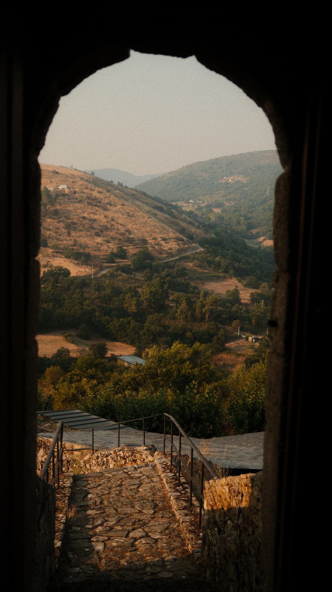 Sunlit mountain valley seen through a dark stone archway