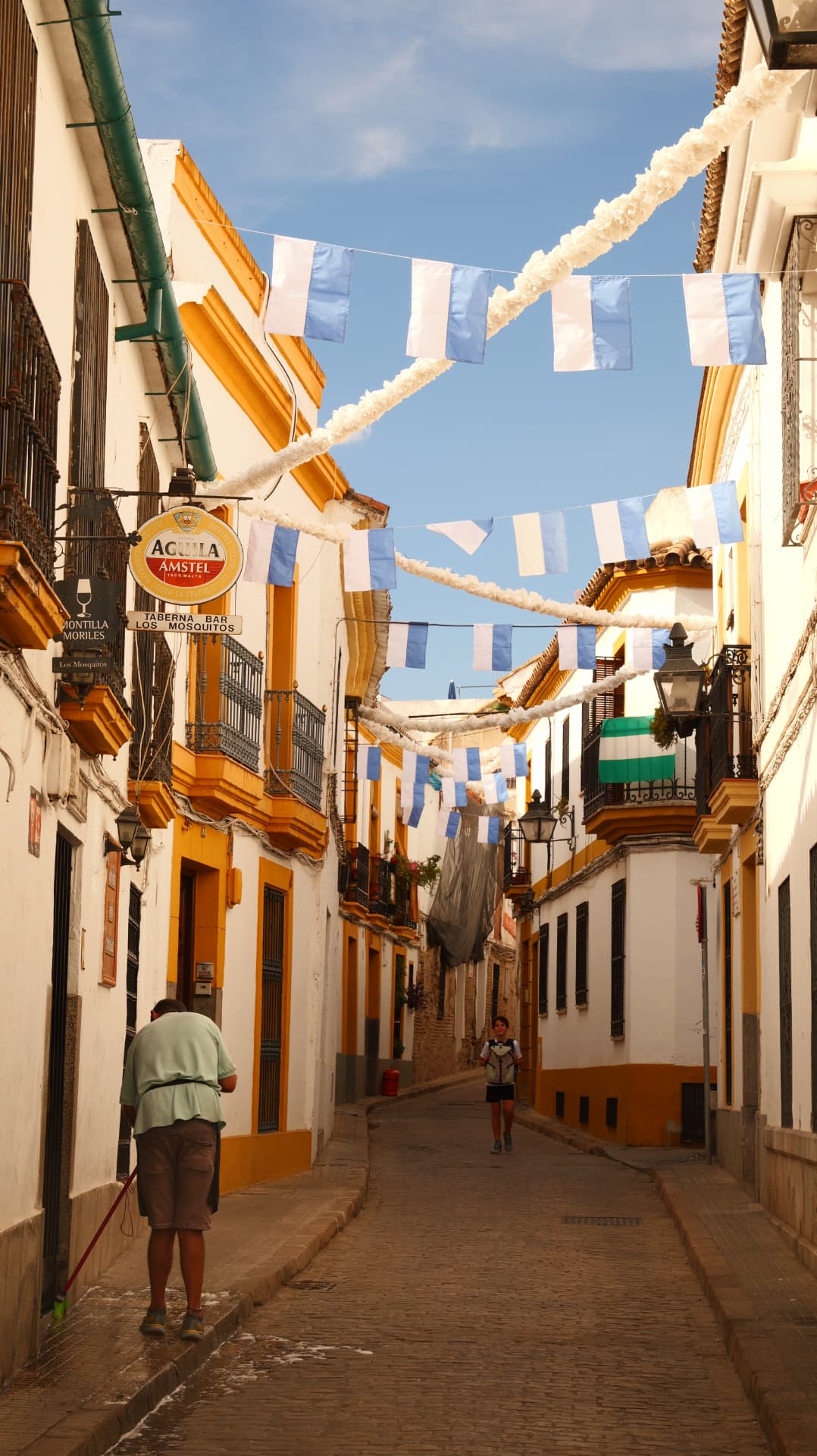Narrow Córdoba street with blue-and-white fiesta flags and a man sweeping the road