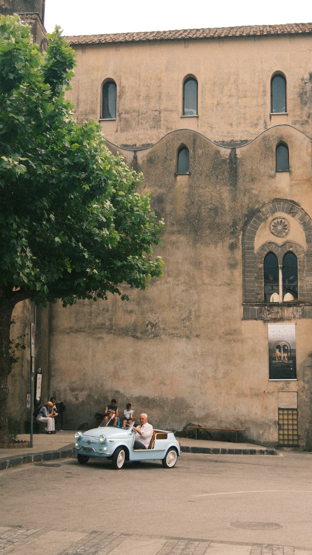 Vintage light-blue Fiat crossing an Italian piazza in front of a stone church