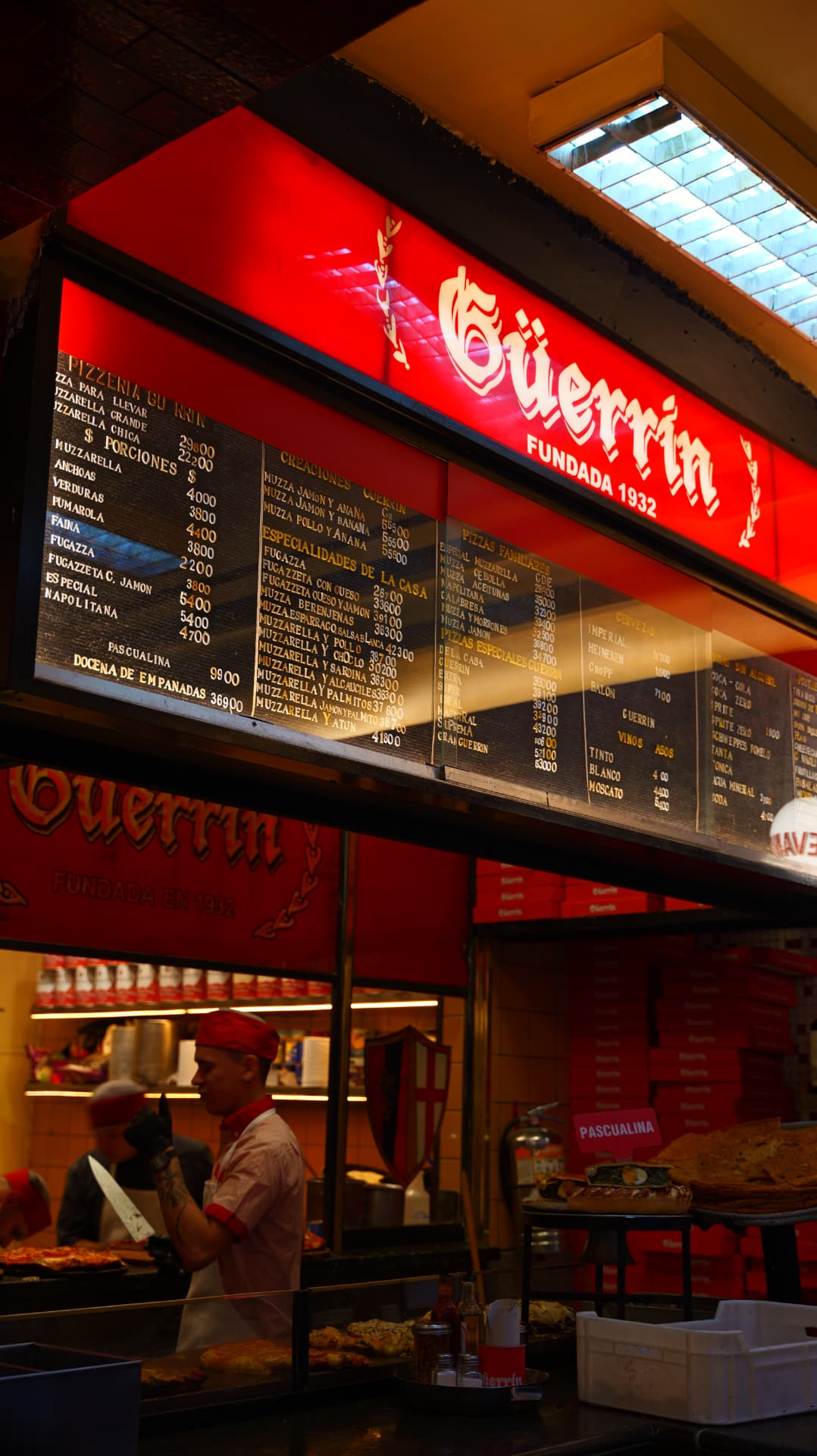 Pizzaiolo at work under the red neon menu boards of Pizzeria Güerrin