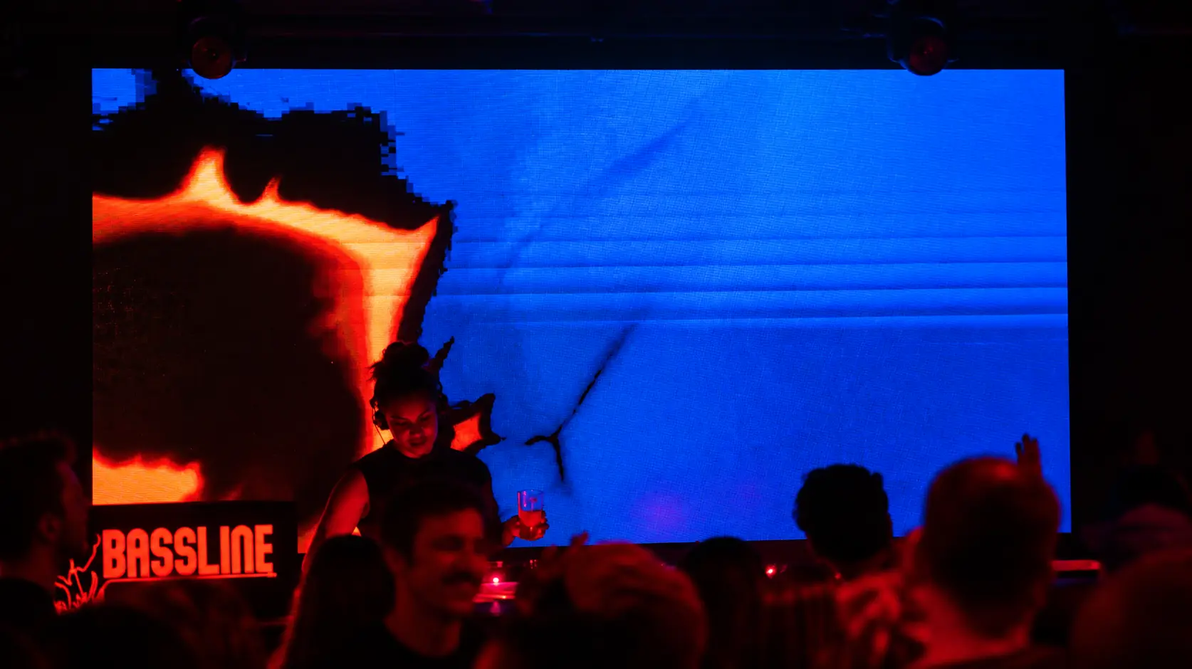 DJ playing in front of a huge blue and red screen at a Bassline party