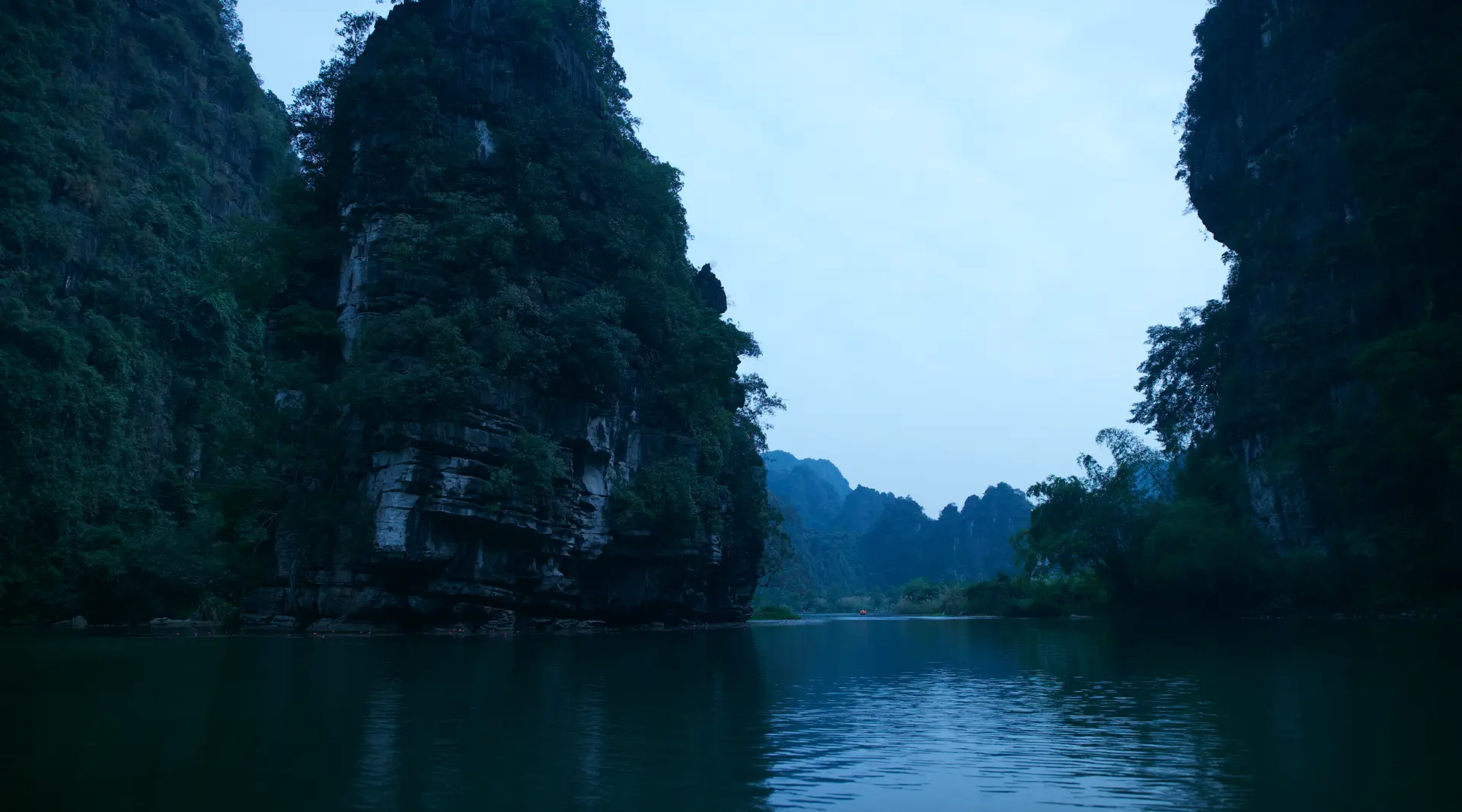 Limestone cliffs rising from still river water at dusk in Vietnam