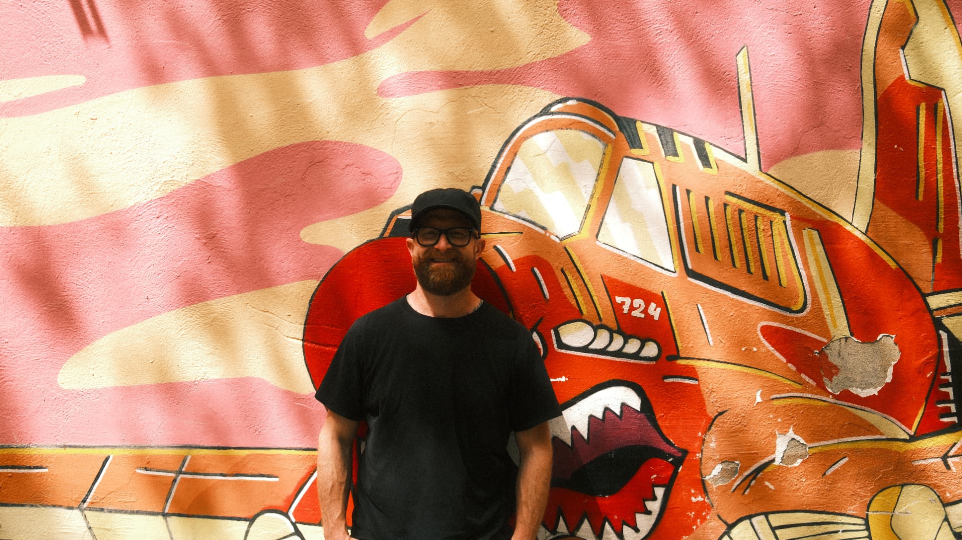 Smiling man in a black cap in front of a painted plane mural