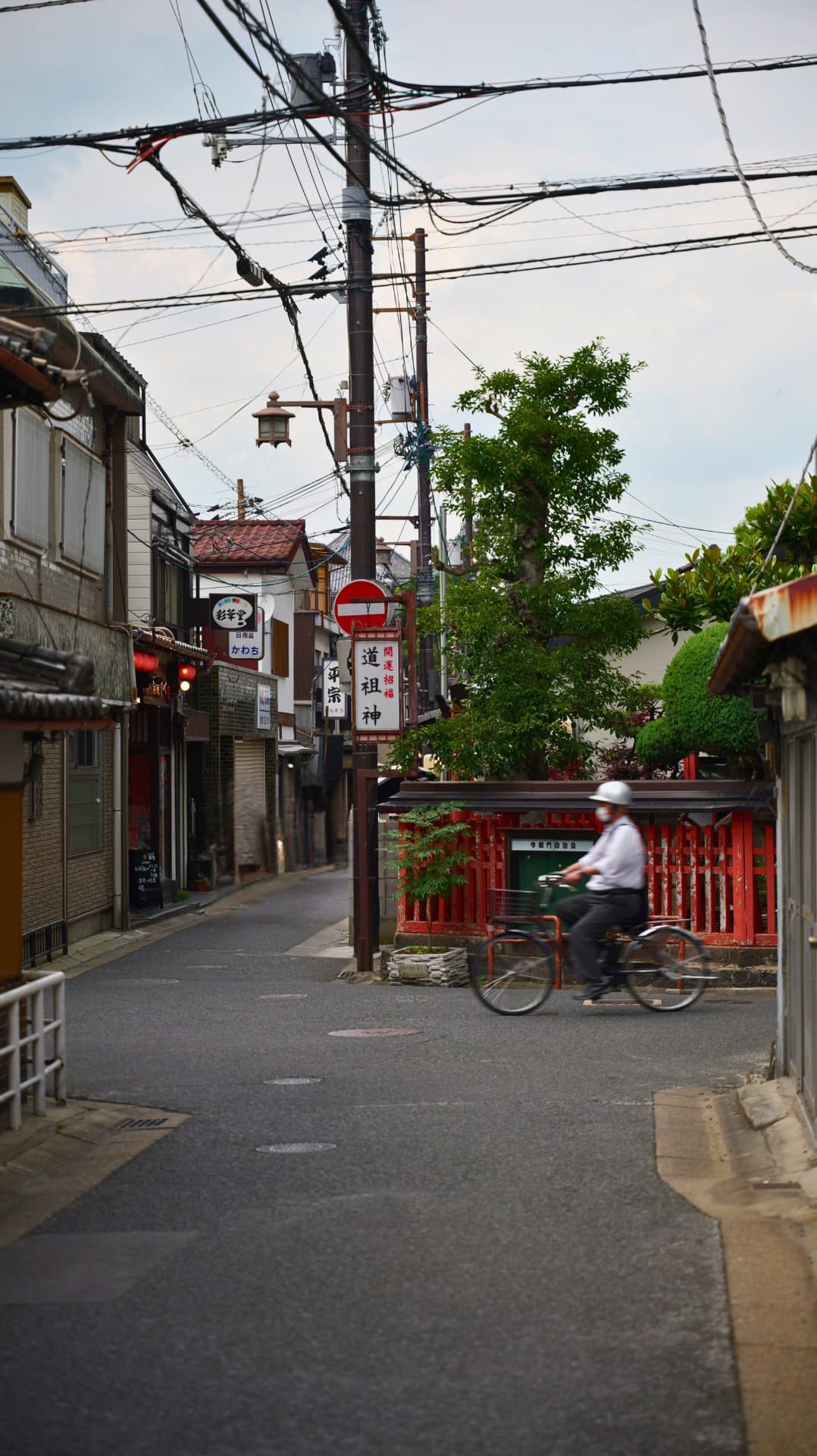 Cyclist crossing a quiet Kyoto backstreet beneath tangled power lines