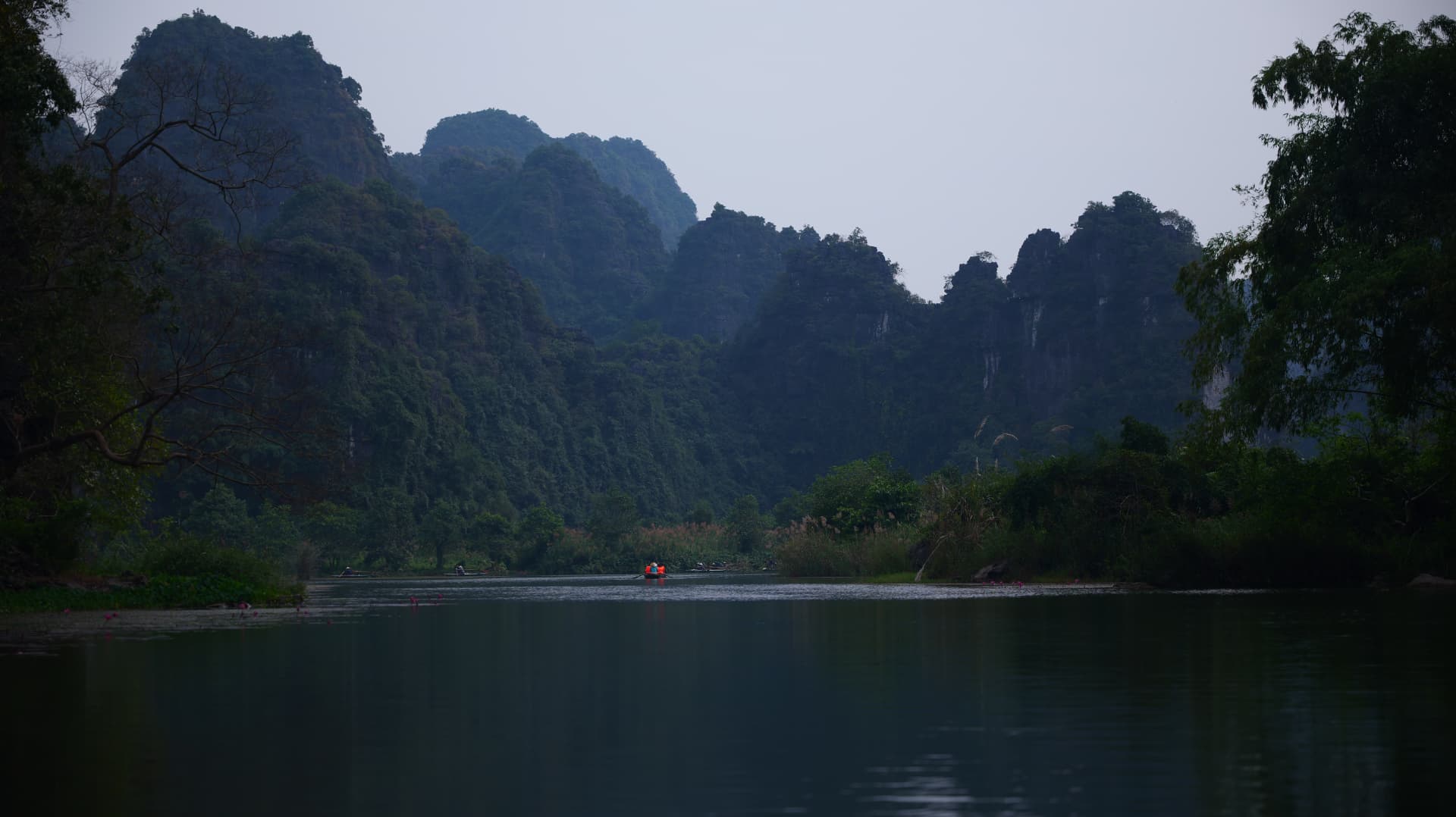 Misty karst peaks above a still river with a lone boat in Vietnam