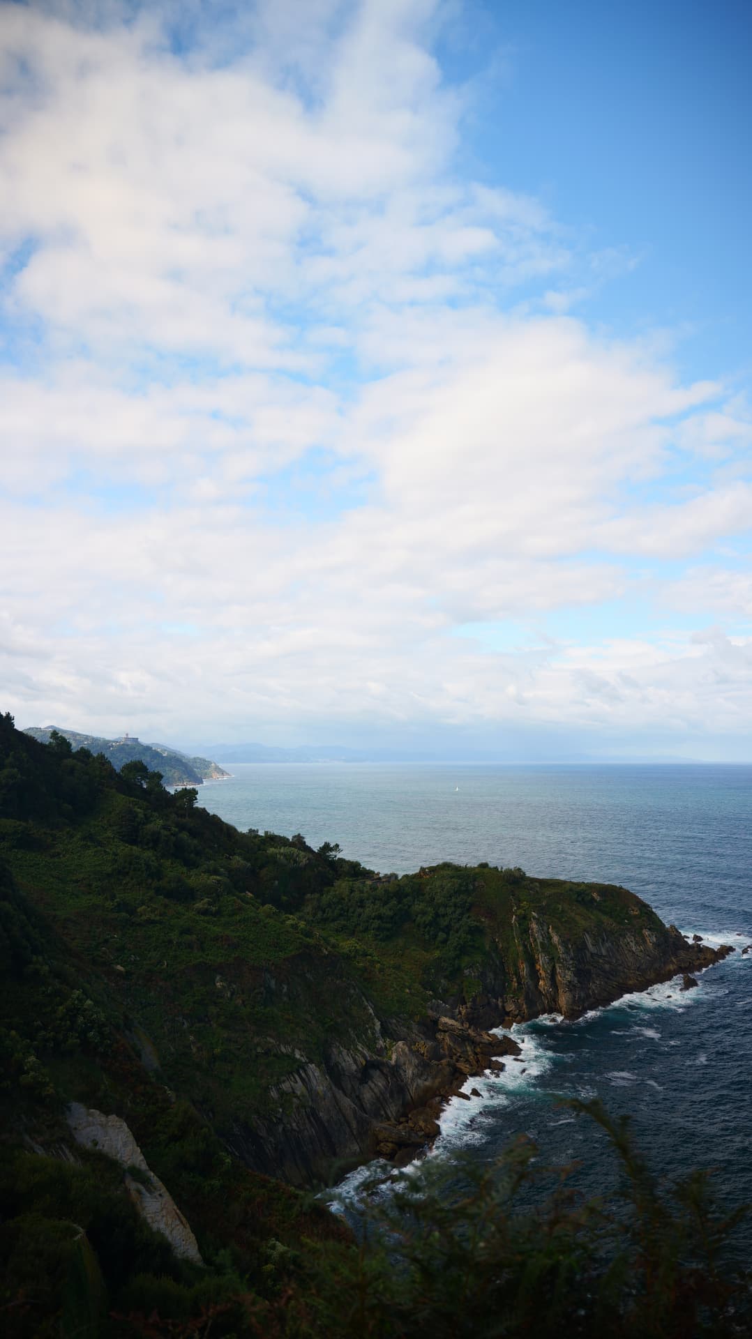 Green cliffs meeting deep blue sea beneath tall clouds on the Basque coast