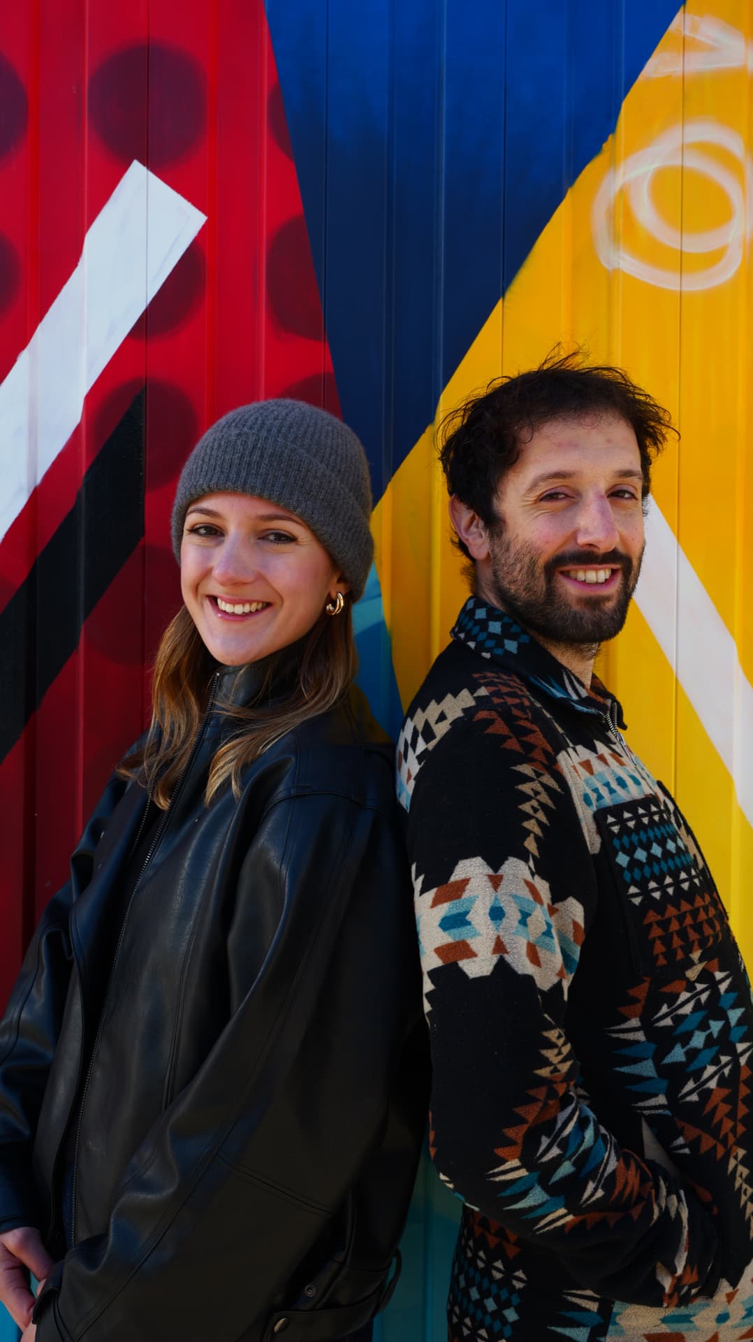 Two people standing back to back in front of a bold painted mural