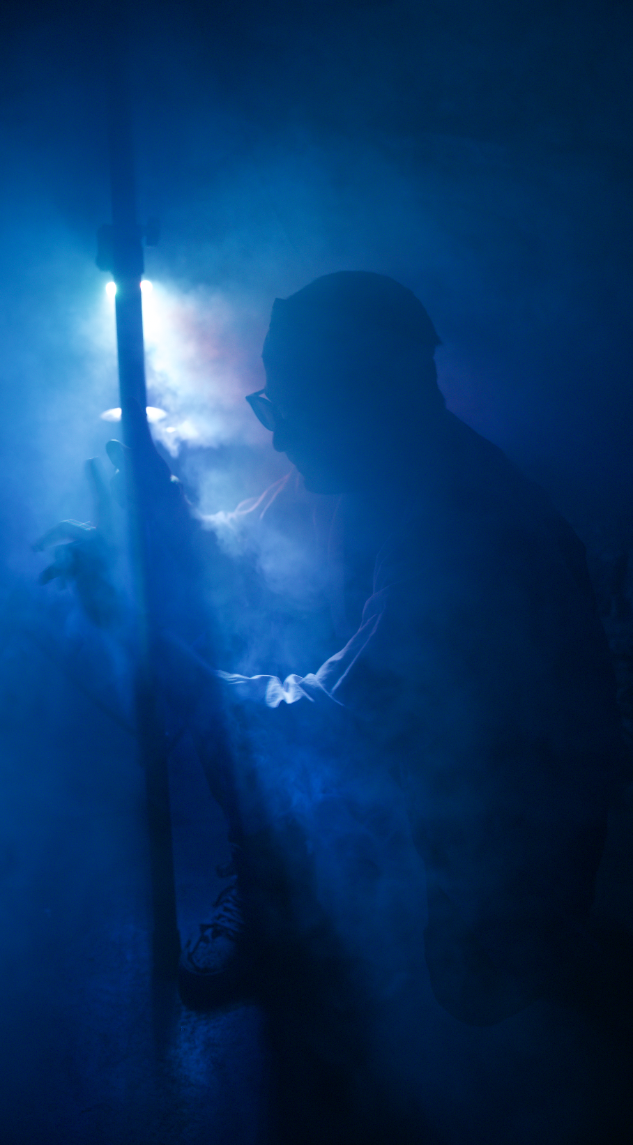 Silhouette of a man crouching in thick blue haze, backlit by cyan light