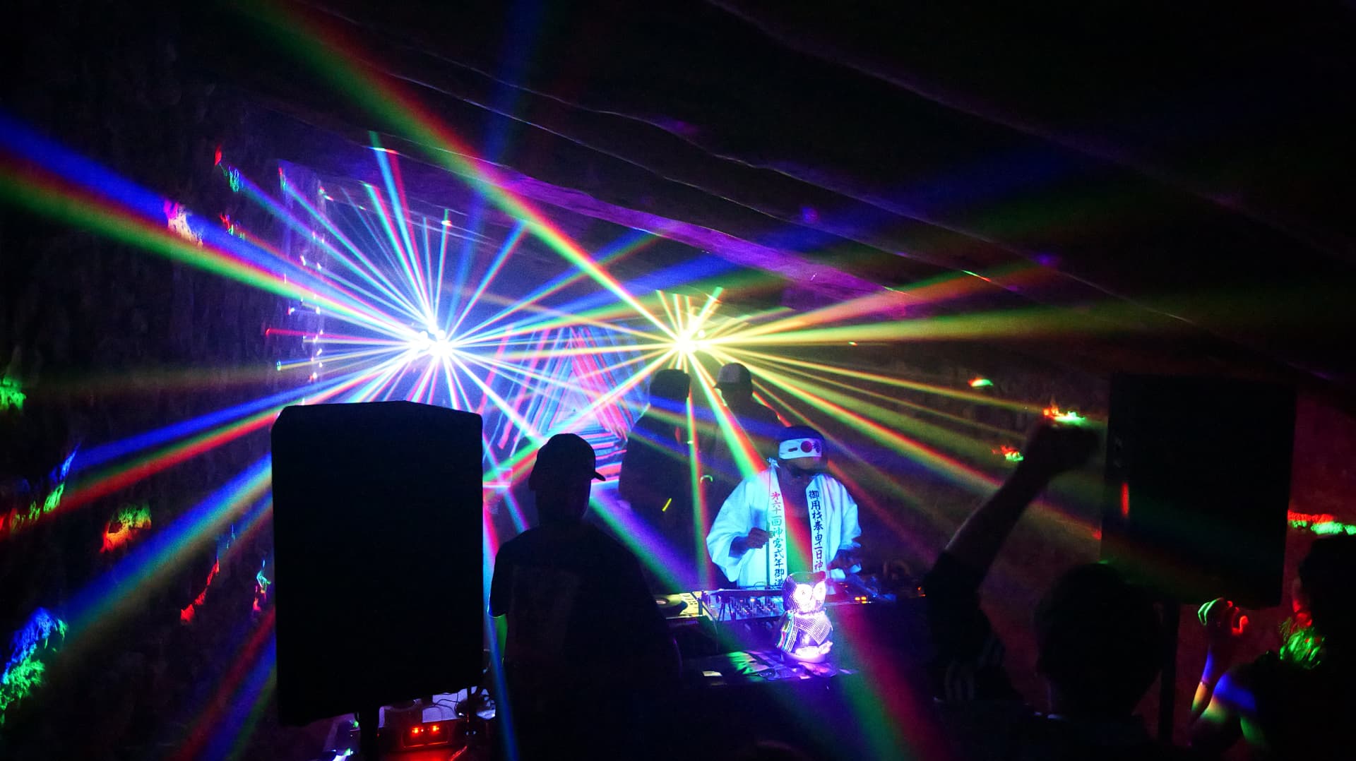 DJ in a white coat mixing amid rainbow laser beams over a club crowd