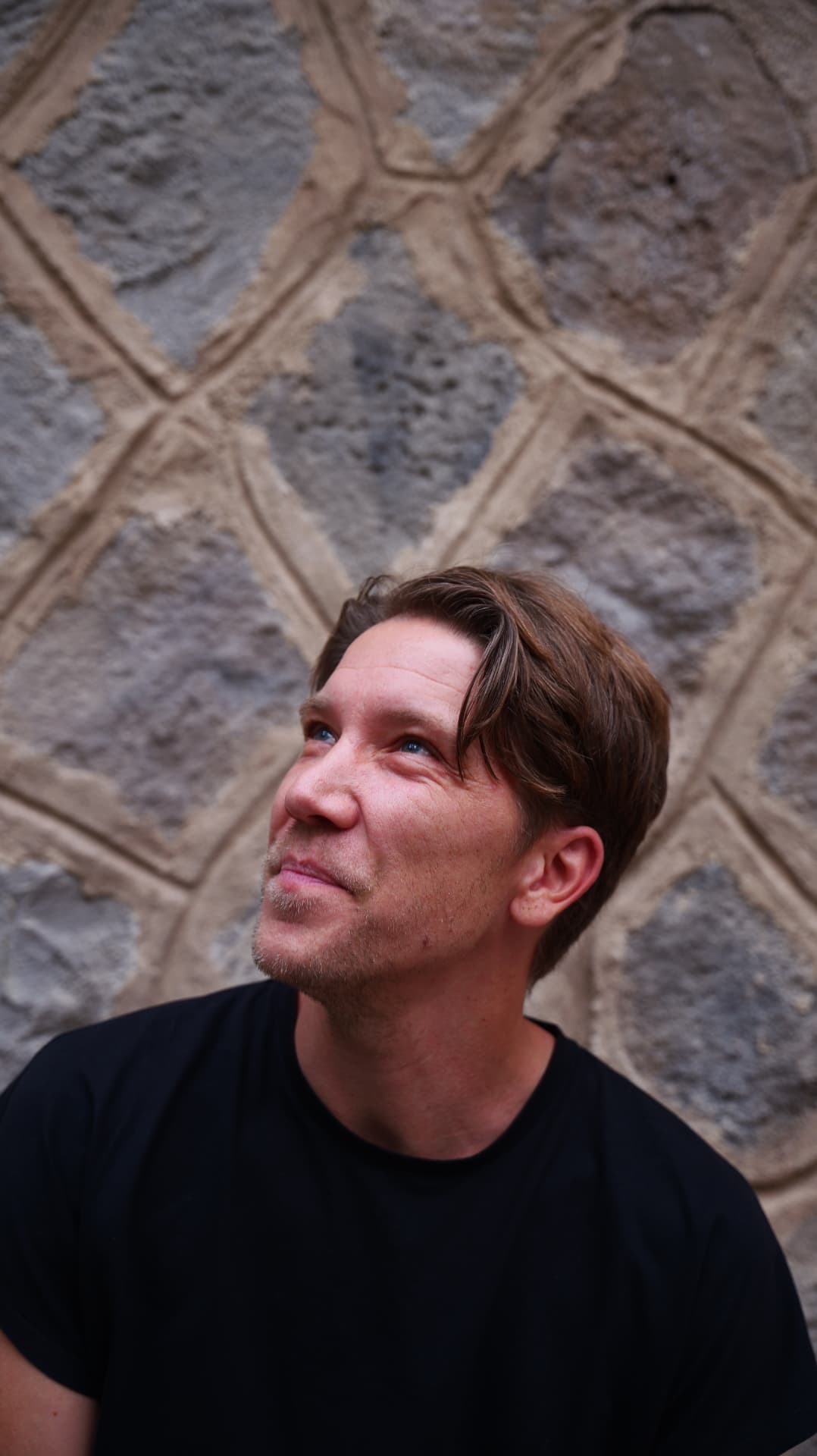 Man in a black t-shirt looking up against a carved stone wall