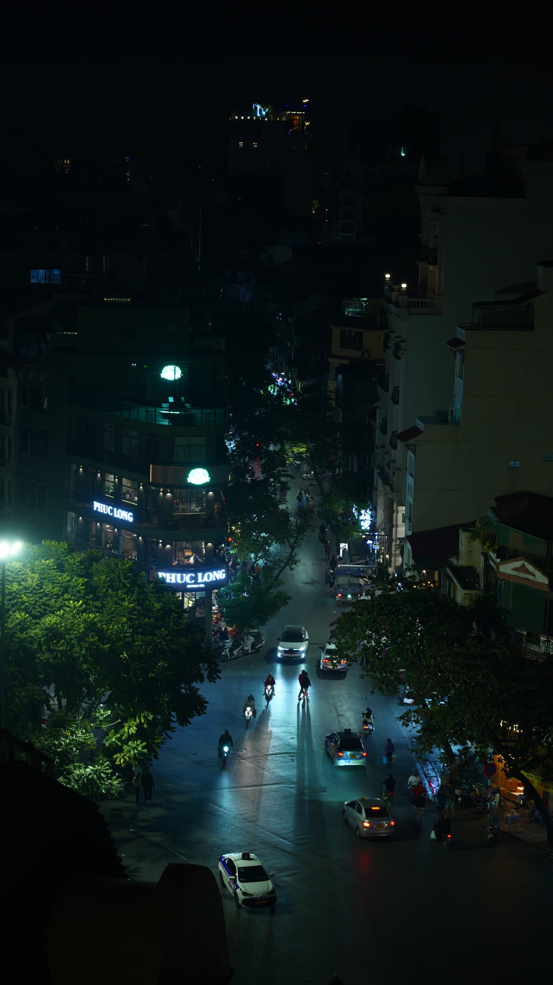 Hanoi street at night seen from above, headlights on wet asphalt