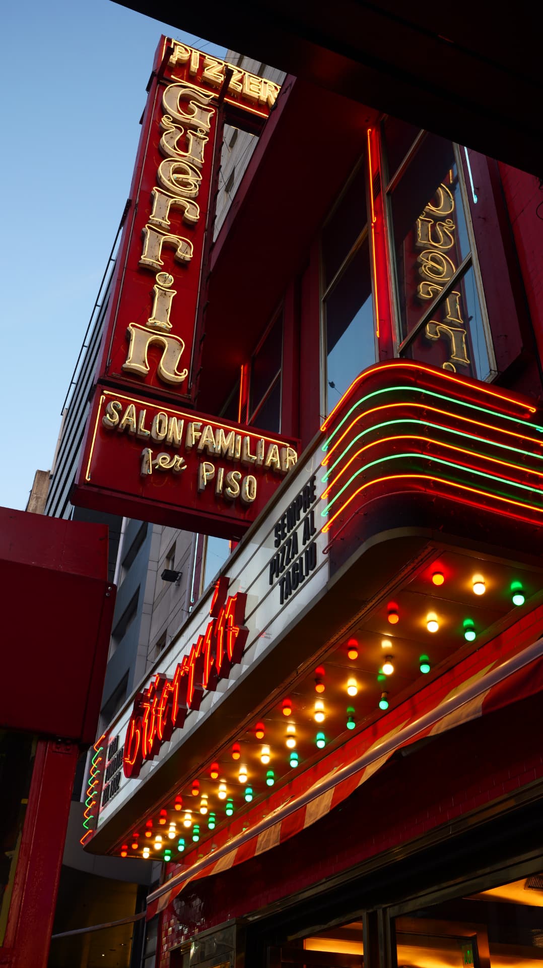Neon sign and coloured bulbs of Pizzeria Güerrin against a blue evening sky