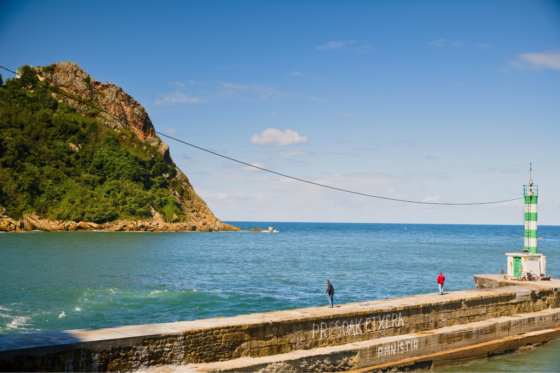Anglers on a breakwater below a wooded hill in San Sebastián