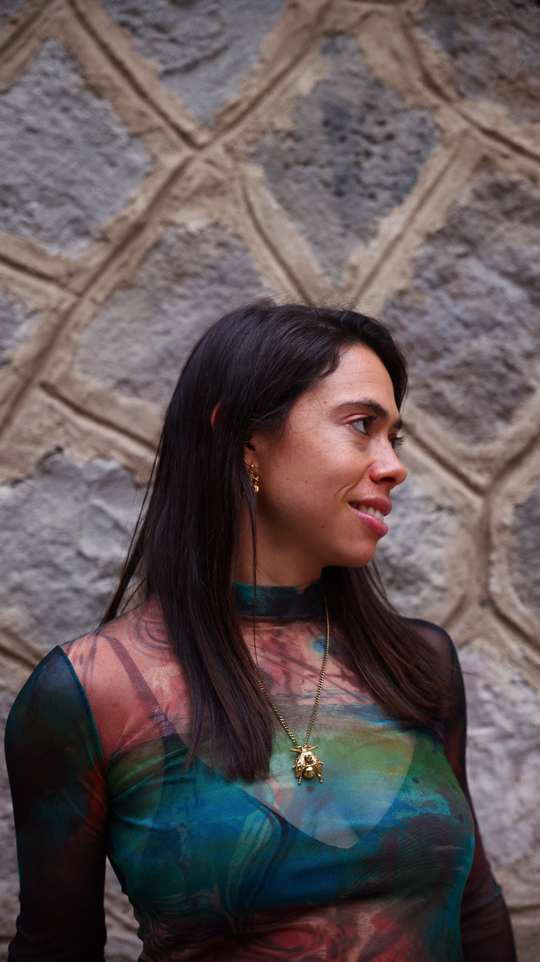 Profile of a woman in a sheer printed top with a gold bee pendant