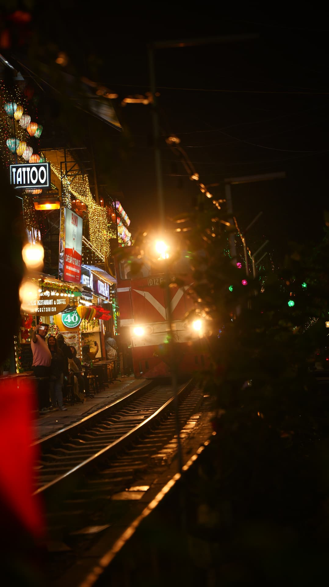 Train passing lantern-lit cafés on Hanoi's train street at night