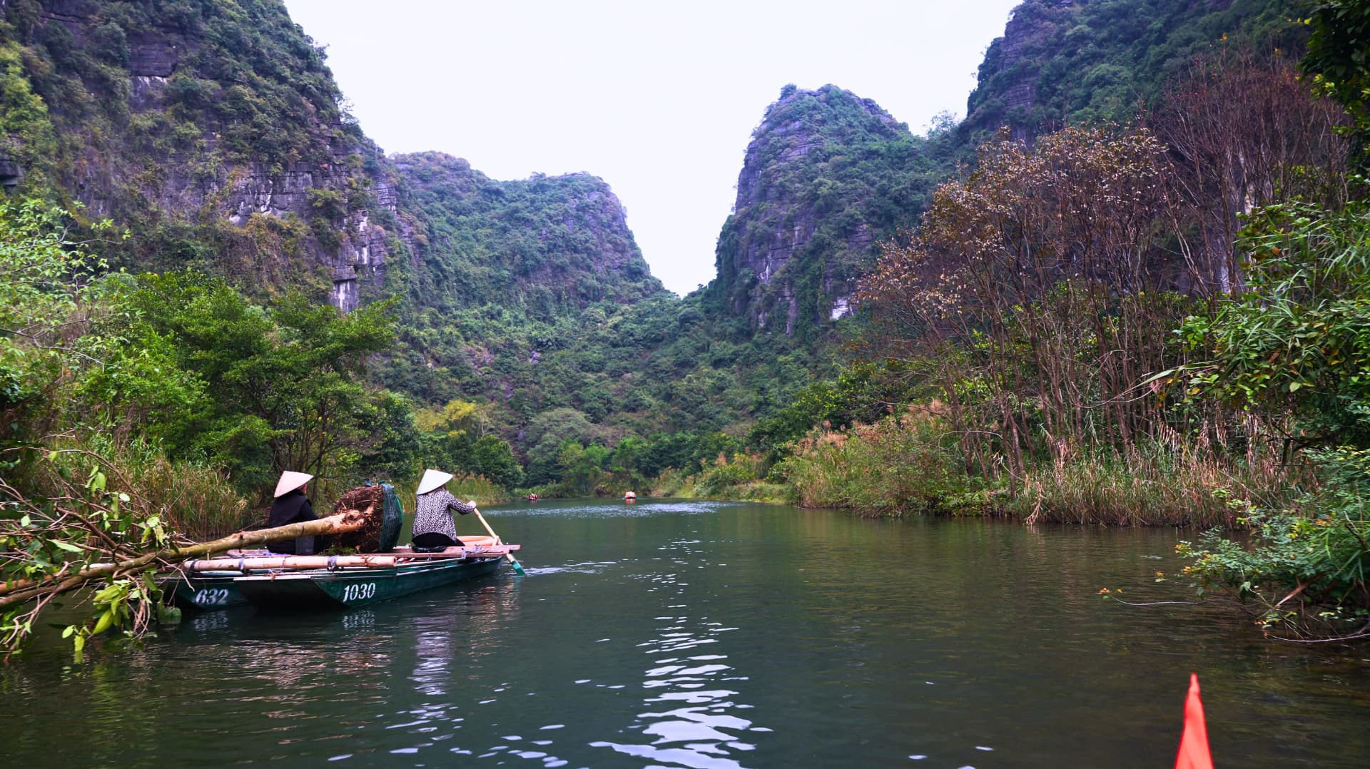 Two rowers in conical hats on a river between limestone karsts in Vietnam
