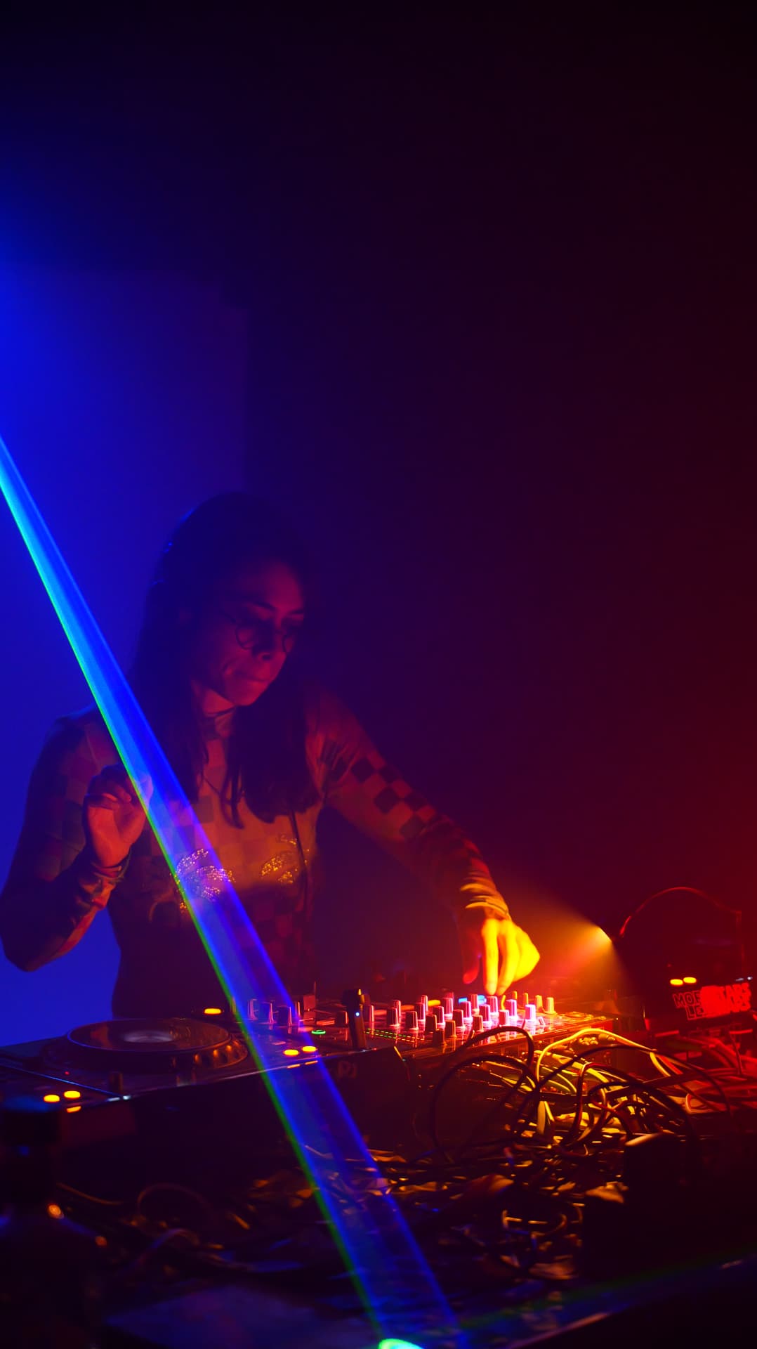 DJ mixing behind the decks as a green laser cuts through blue and red haze