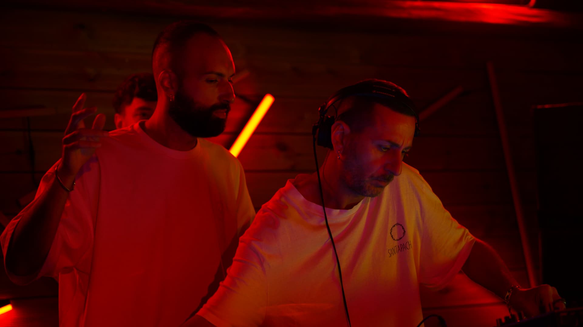 Two DJs side by side in deep red light behind the decks
