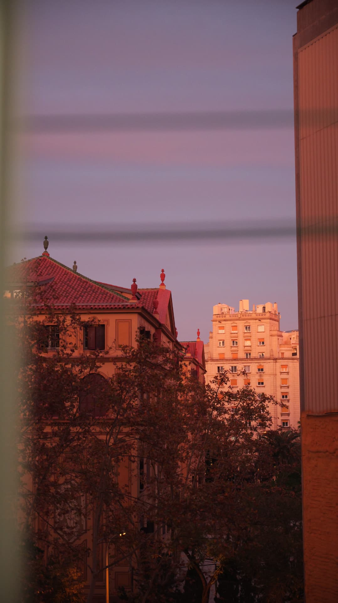 Barcelona rooftops glowing pink at sunset seen past a building edge