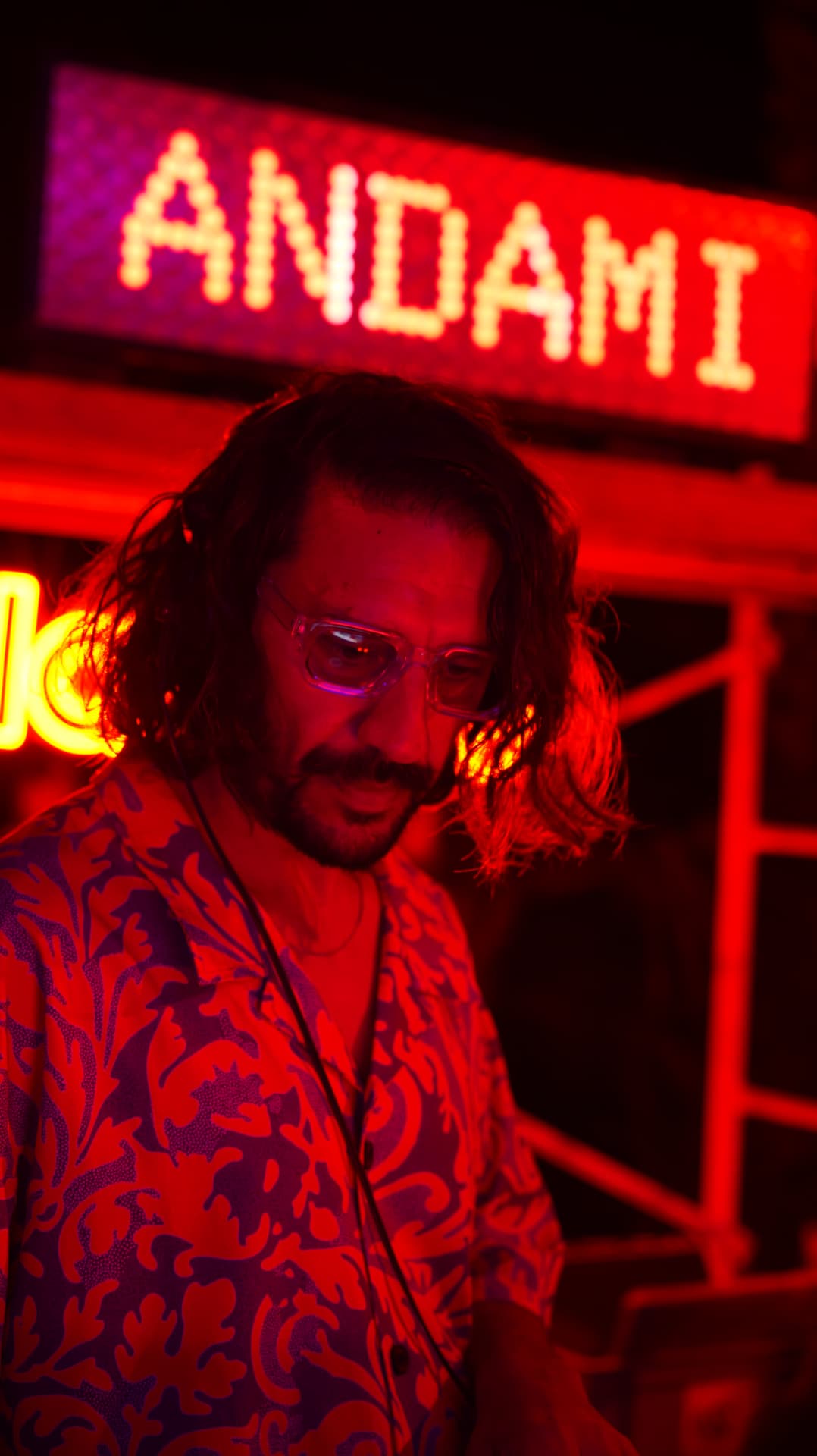 DJ lit in red beneath a glowing ANDAMI LED sign