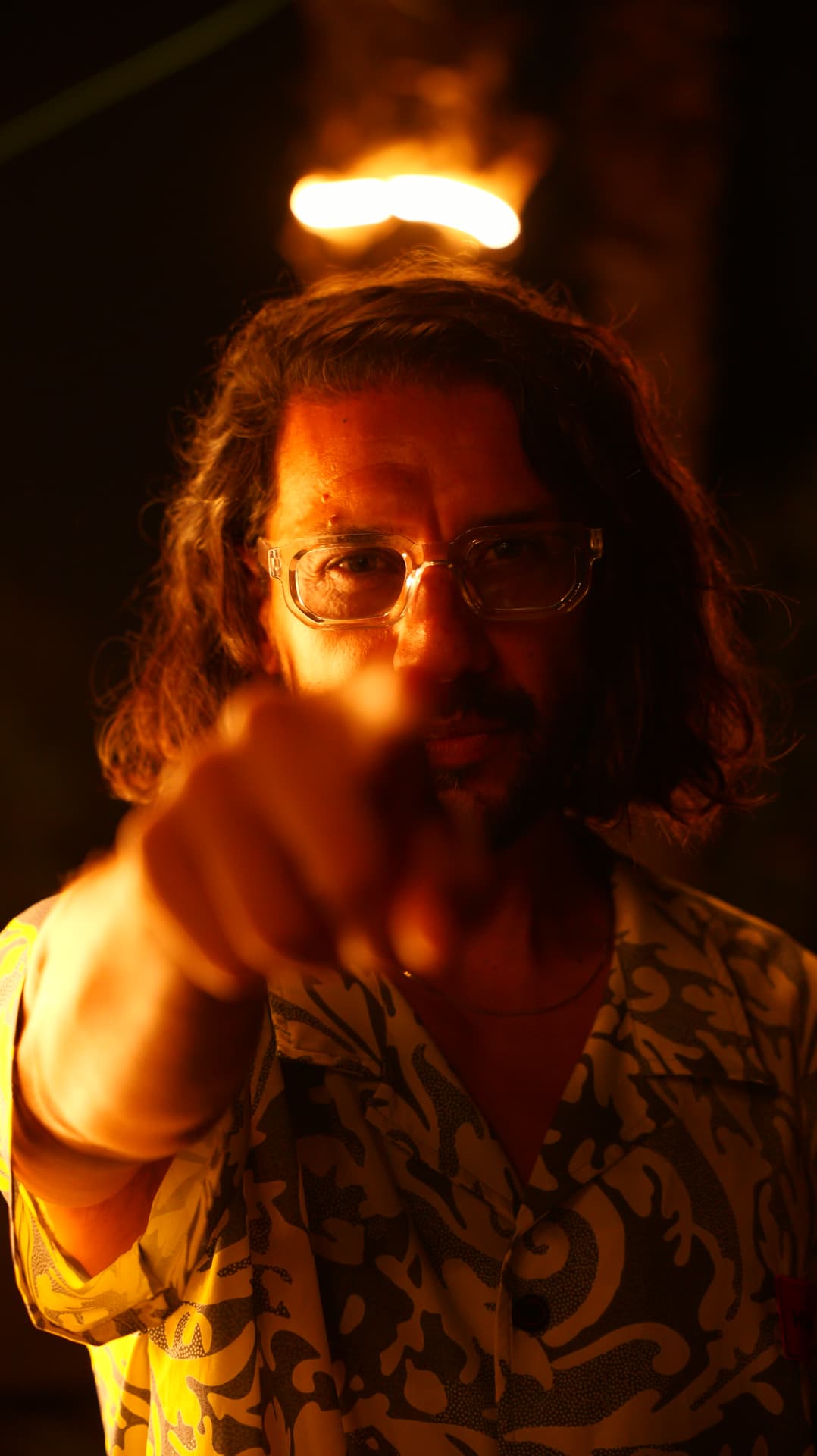 Man pointing at the camera under a flame, lit in deep orange