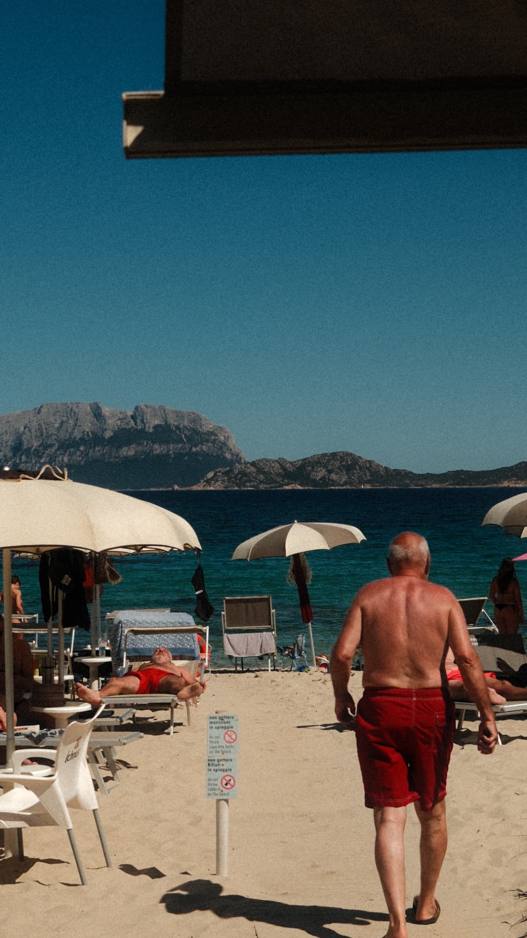 Man walking between beach umbrellas toward the sea and Tavolara island