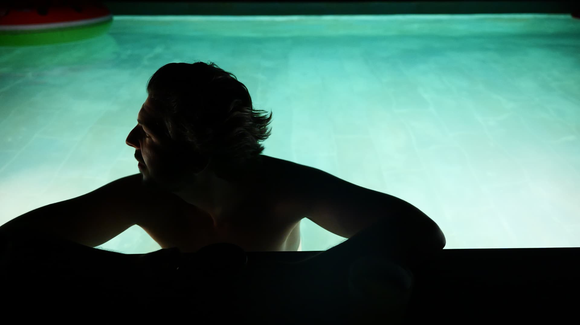 Silhouette of a man resting at the edge of a glowing turquoise pool