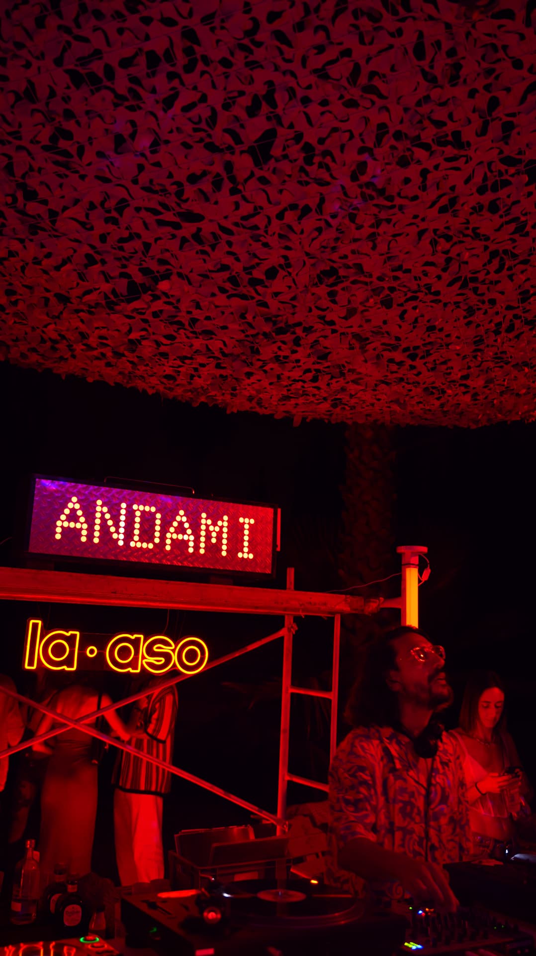 DJs playing vinyl beneath camouflage netting and red party light