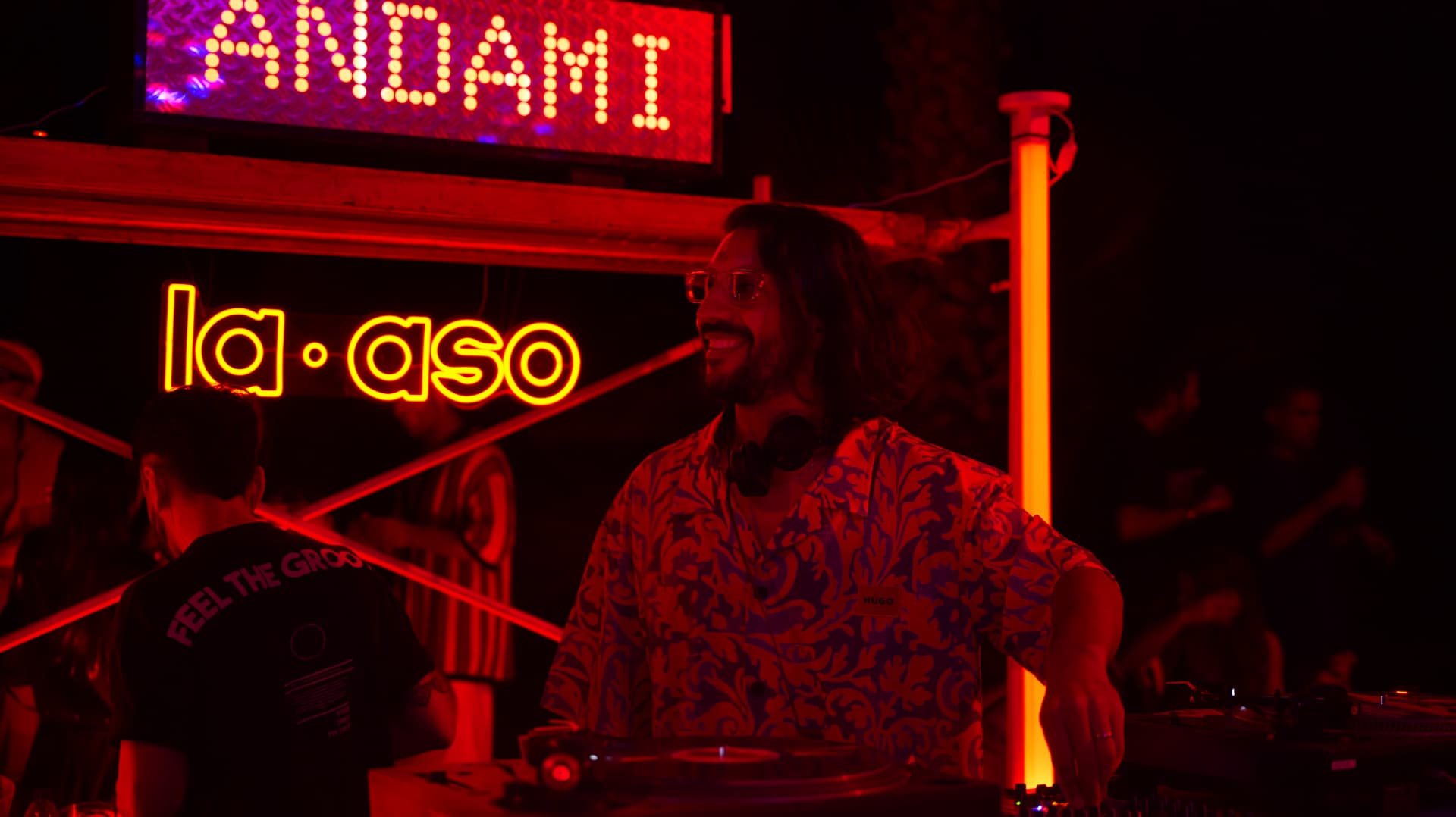 Smiling DJ over the turntables under warm neon club signage