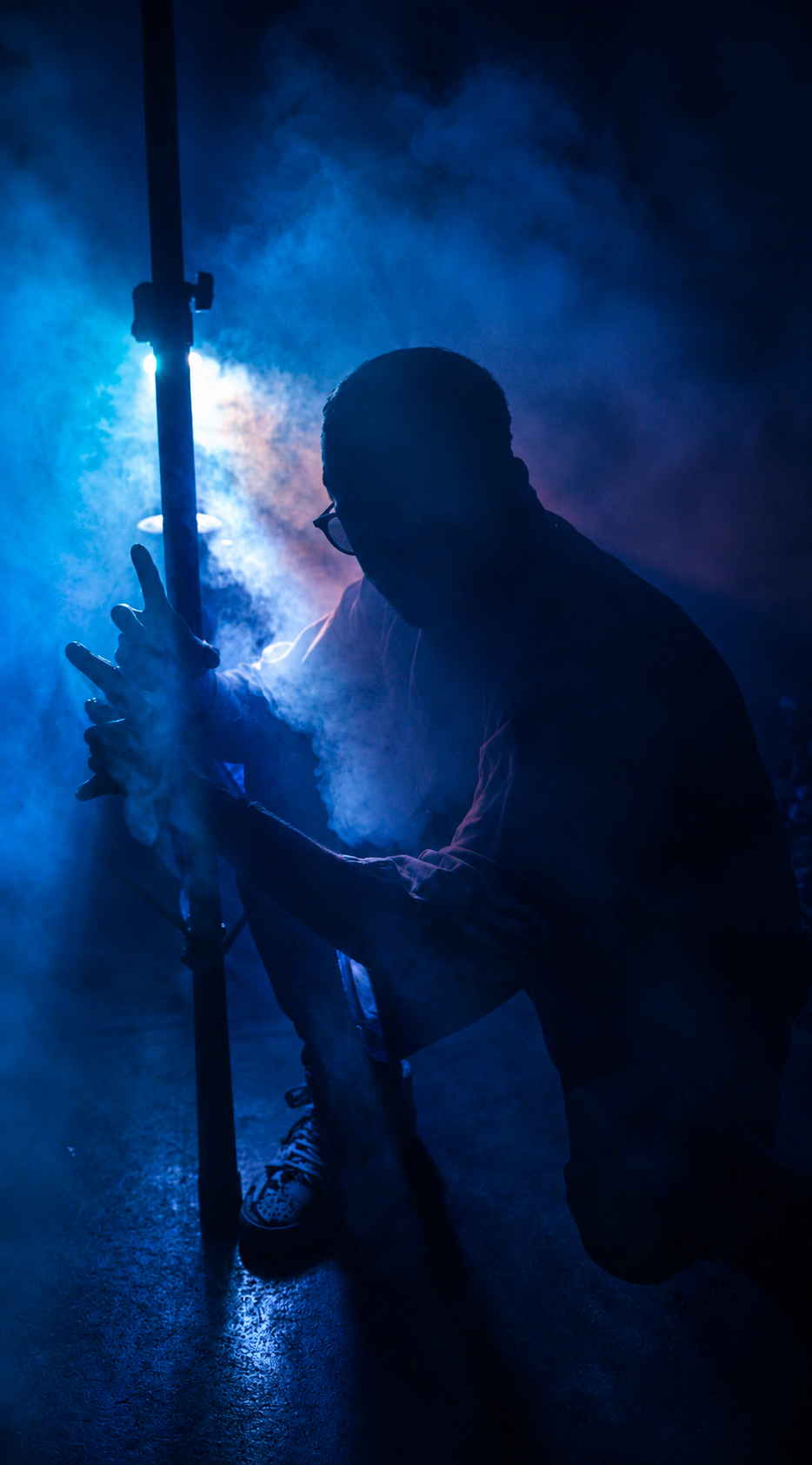 Silhouette of a man crouching among blue smoke under a glowing light stand
