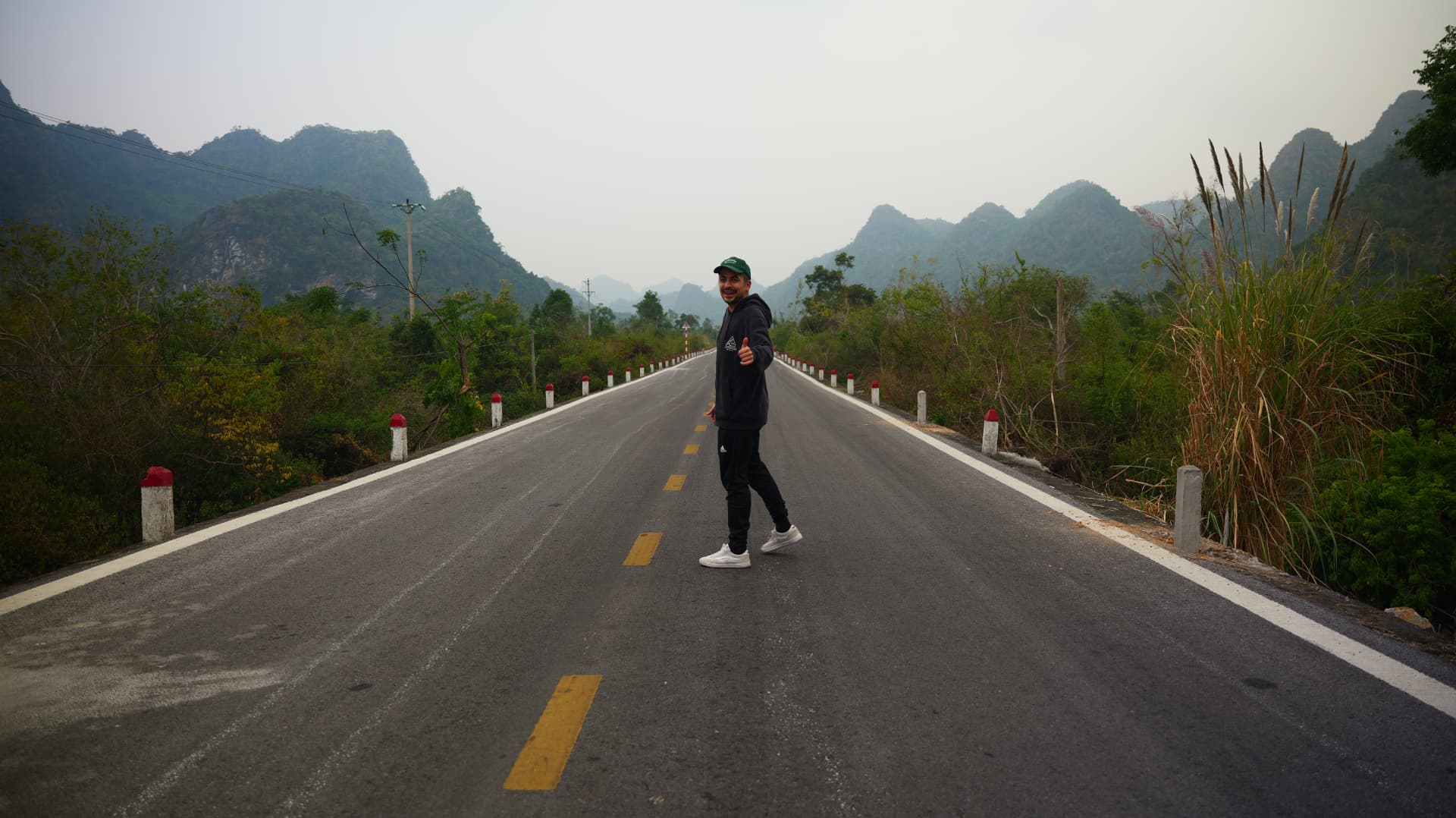Alex standing on an empty road between misty limestone mountains in Vietnam