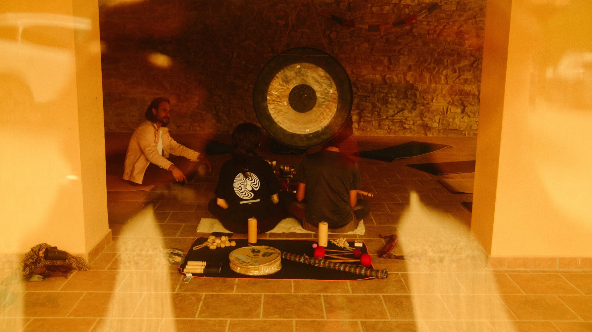 Three people around a large gong during a sound ceremony in warm light