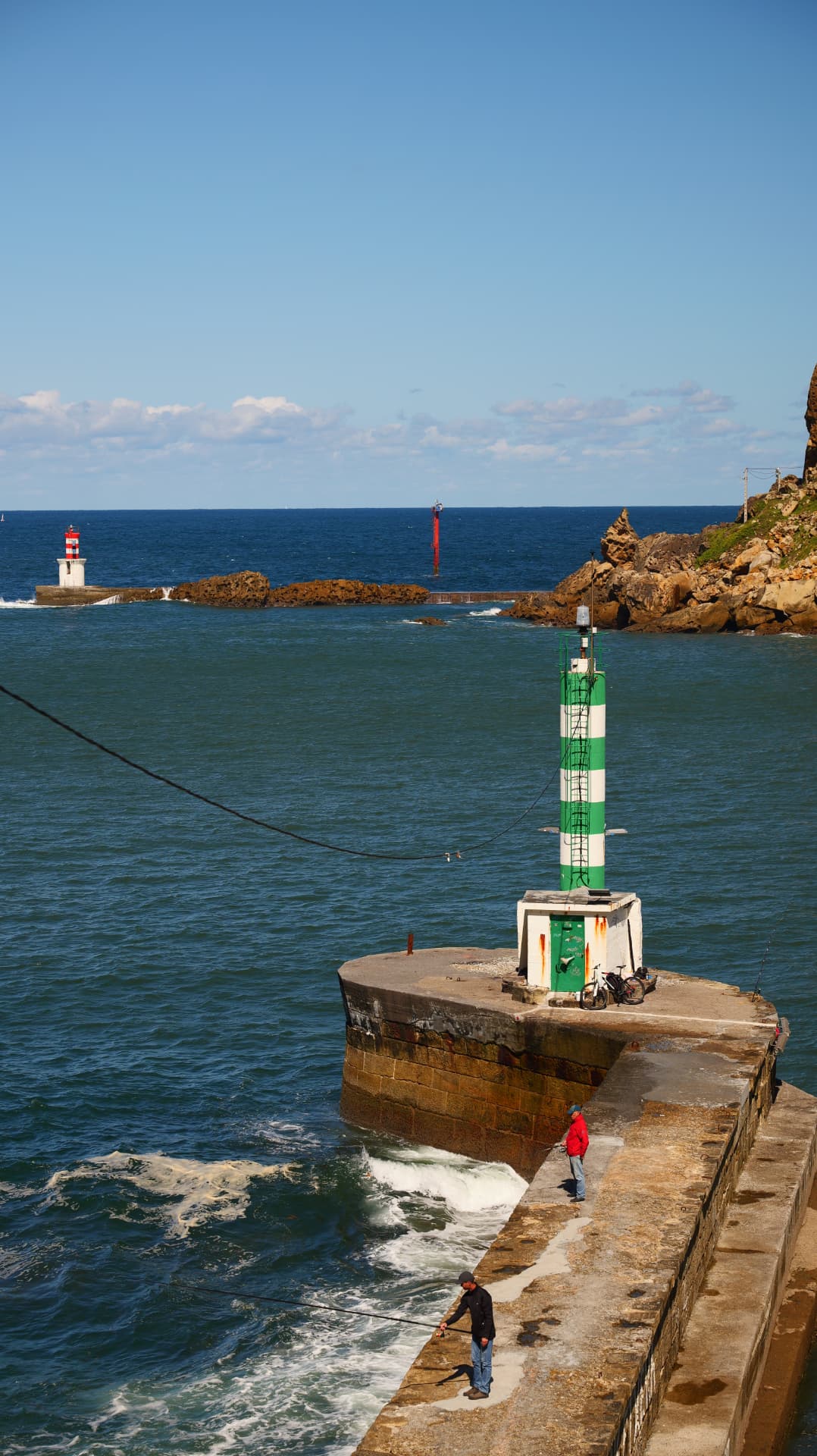 Fishermen on a harbour breakwater with green and red lighthouses at the sea entrance