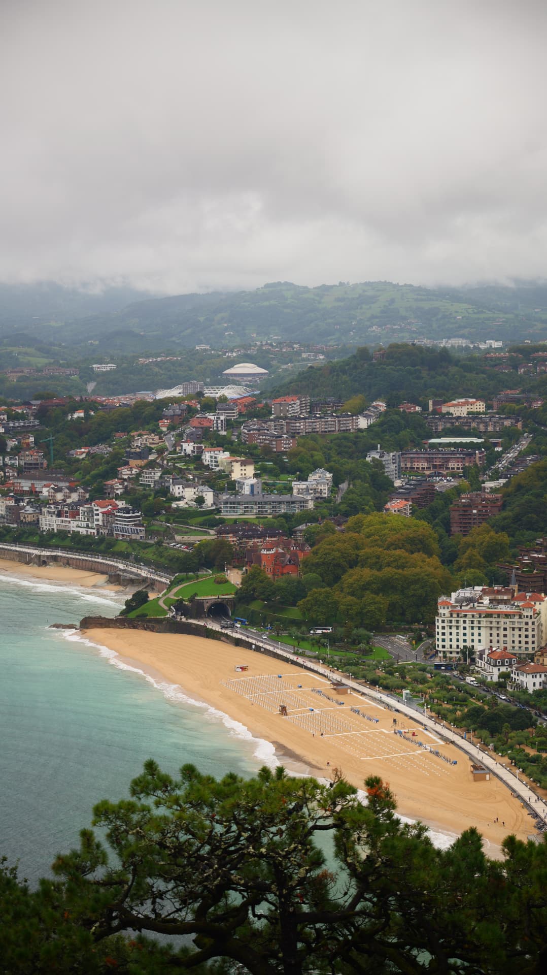 Aerial view of San Sebastián's beach and hillside town under low cloud