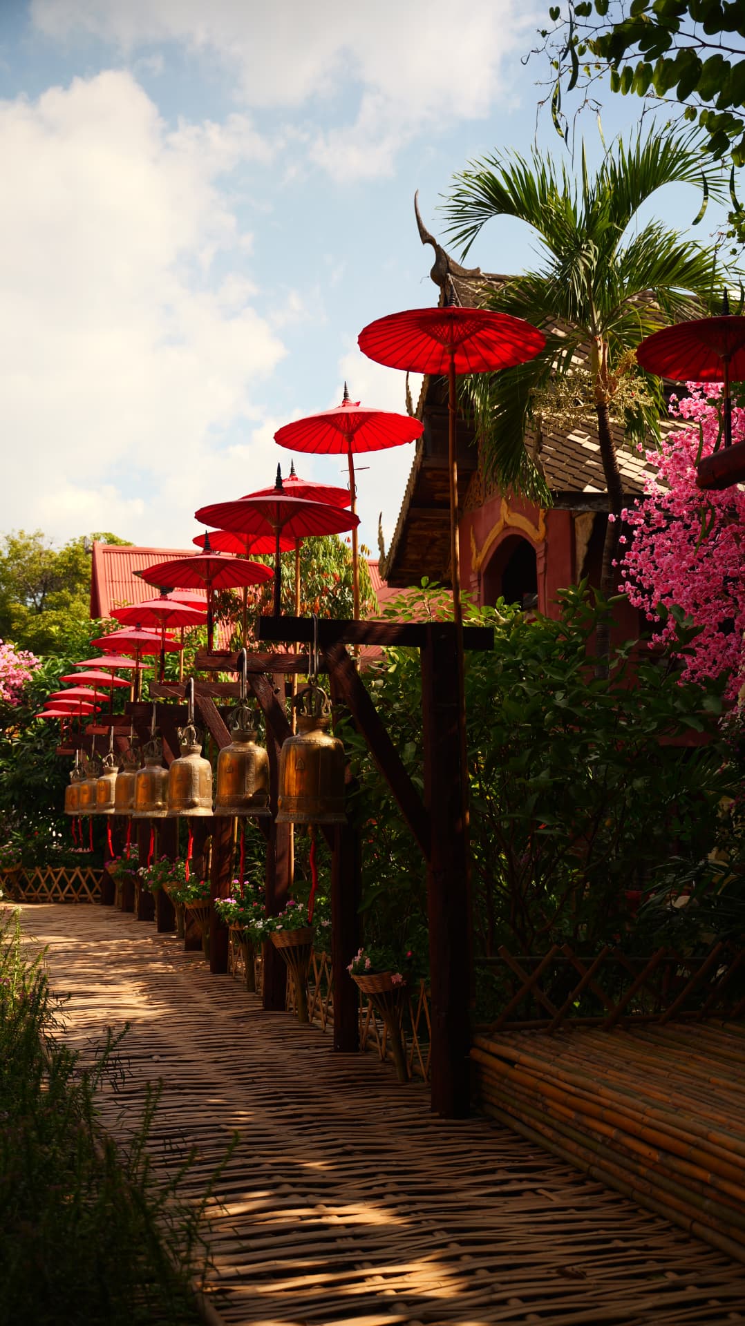 Red parasols and brass temple bells along a bamboo walkway in Thailand