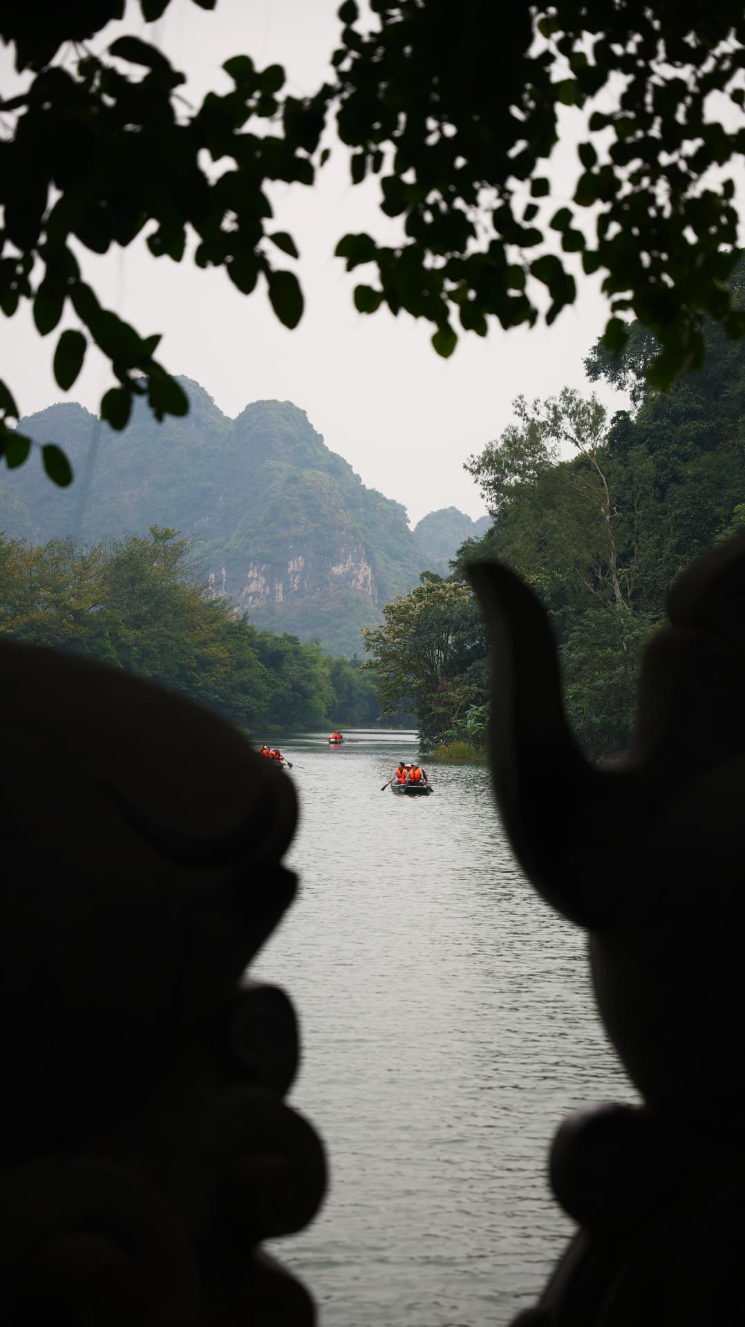 Boats crossing a Vietnamese river beneath karst mountains, framed by temple silhouettes