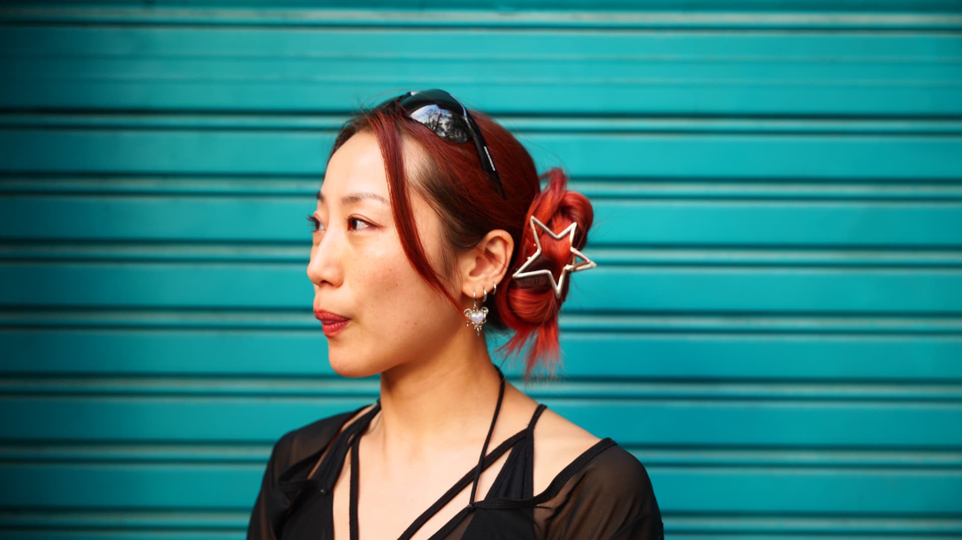 Profile of a woman with red hair and a star hair clip against a teal shutter
