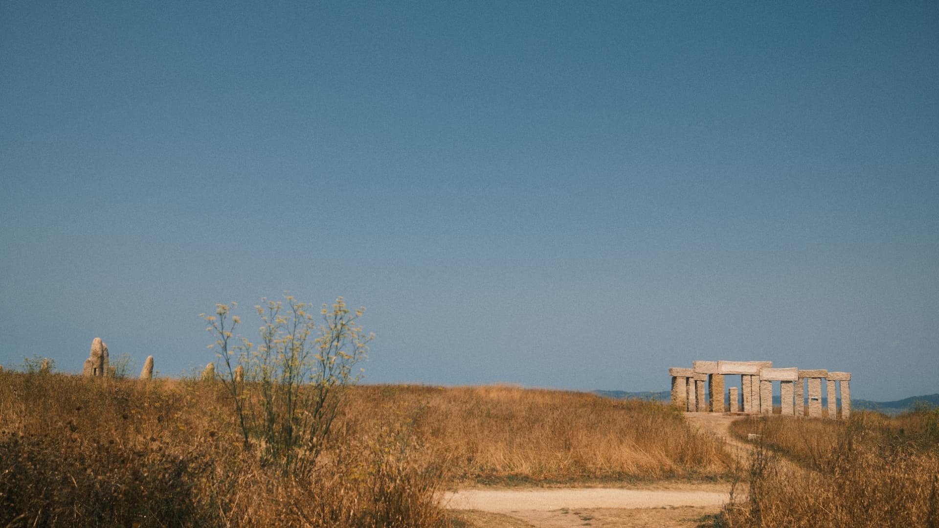 Stone circle standing above golden dry grass under a clear blue sky
