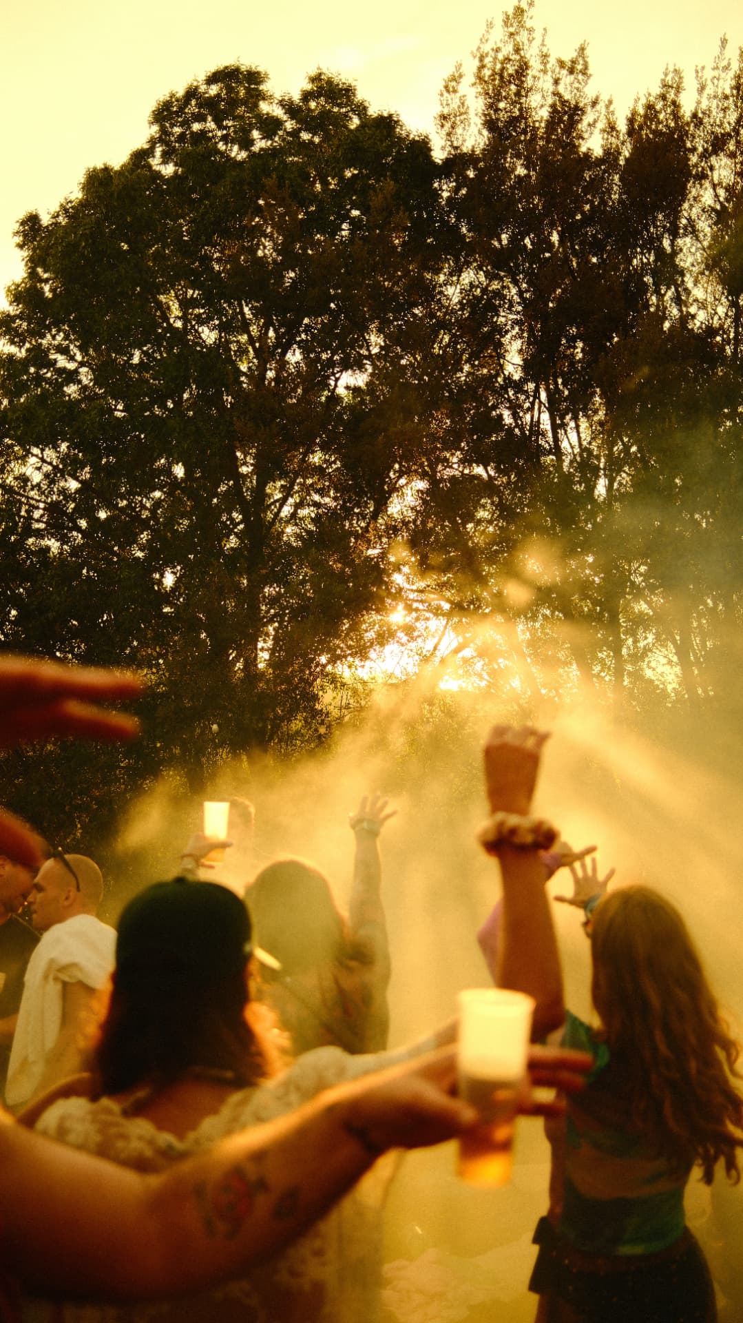 Dancers with raised hands in water mist and golden sunset light